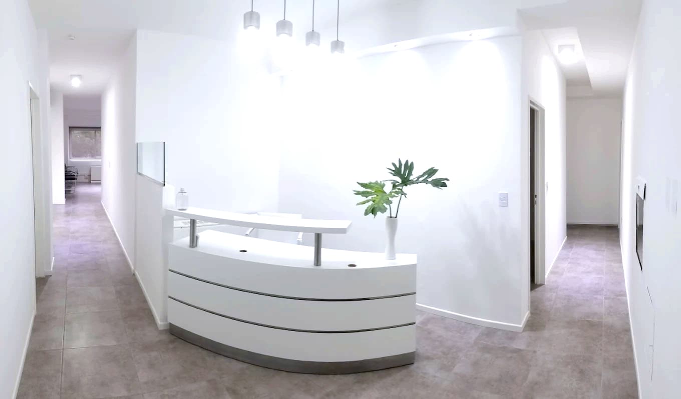 Recepción de PC Dental Studio: mostrador curvo blanco con detalles cromados y piso de piedra gris